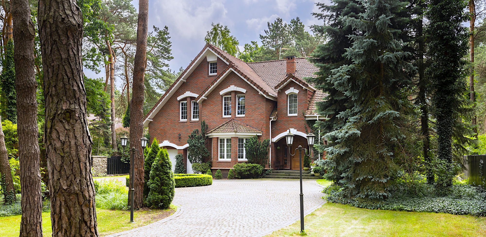Large, rural estate with brick facade and green lawn standing in the forest among trees